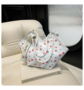 Detail of white cherry print tote bag with woven shoulder strap on a beige sofa