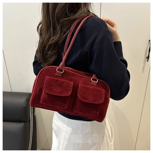 Detail of burgundy suede shoulder bag featuring dual front pockets and long round handles