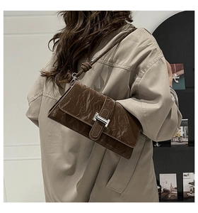 Detail showing the vintage brown textured shoulder bag with silver H-shaped buckle on a trench coat