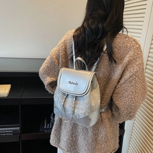 Silver metallic mini backpack with chain and cat print, worn by a model in a library