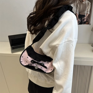 Pink pleated underarm bag with black bows and heart pendant shown on model