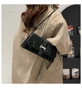 Détail d'un sac à bandoulière en cuir plissé noir avec boucle en H sur manteau beige