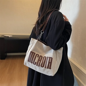 Minimalist canvas tote bag with brown MCROIR lettering and metal chain strap on model