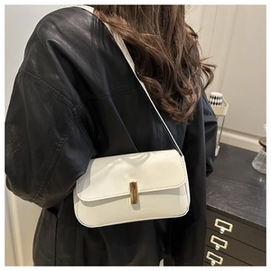 Close-up of a white patent leather shoulder bag with a gold buckle worn by a model