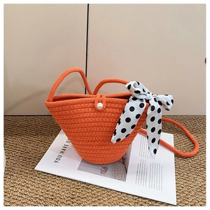 Détail d'un sac seau tressé orange avec fermoir perle et foulard en soie à pois noir
