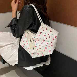 White tote bag with red cherry prints and branded wide shoulder strap shown on a model