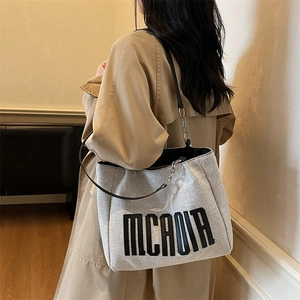 Large cream canvas tote bag with black letters and chain strap worn by a model