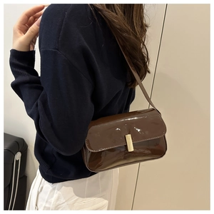 Detail of a brown patent leather shoulder bag featuring a gold rectangular metal lock