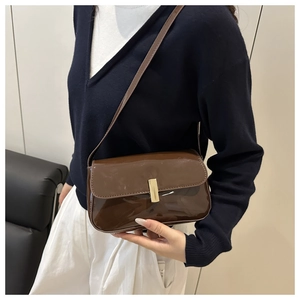 Detail of dark brown patent leather shoulder bag with sleek gold buckle on model