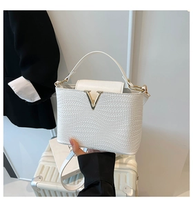 Detail of white woven texture crossbody bag with gold V-shaped logo and top handle