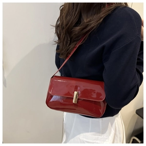 Close-up of a burgundy patent leather shoulder bag with a gold clasp on a model