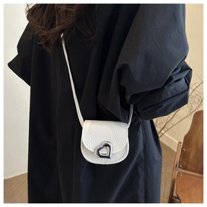 Détail du sac selle en cuir grainé blanc avec boucle cœur argentée porté par un mannequin