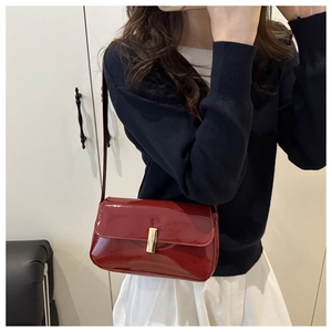 Detail of red patent leather crossbody bag with vertical gold lock on a model
