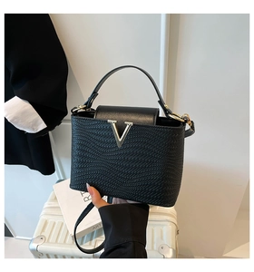 Detail of black woven shoulder bag with gold V-hardware and adjustable strap on luggage