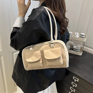 Beige canvas shoulder bag with white leather trim and double pockets in a home setting