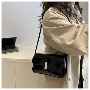 Detail of glossy black patent leather shoulder bag with elegant gold rectangular buckle