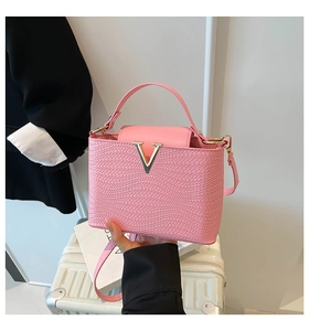 Close-up of pink woven handbag featuring a signature gold V-shaped metal buckle detail