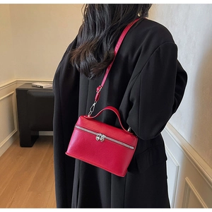 Detail of red vanity cross-body bag with heart zippers worn over a black coat