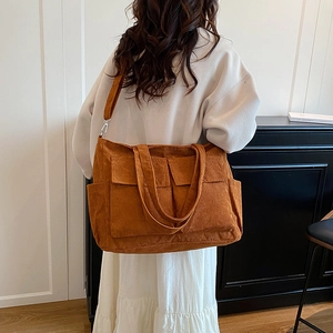 Large brown corduroy tote bag with multiple pockets worn by a model in a minimal setting