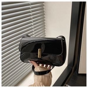 Detail of black patent leather shoulder bag with a polished gold rectangular metal buckle