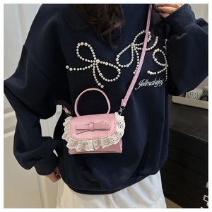 Detailed shot of pink PU leather crossbody bag with white lace trim and bow accent