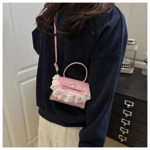 Close-up of pink crossbody bag featuring decorative leather bow and white lace embroidery