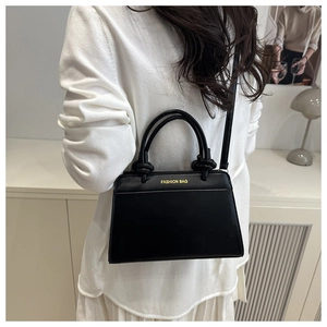 Detail of black trapezoid PU leather bag with knotted handles and gold lettering