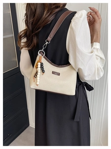 Detail of off-white canvas hobo bag with dark brown leather trim and beaded pendant