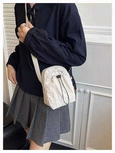 Detail of a cream drawstring crossbody bag with embroidered logo and shoulder strap