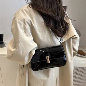 Glossy black patent leather shoulder bag with gold clasp shown on a trench coat model