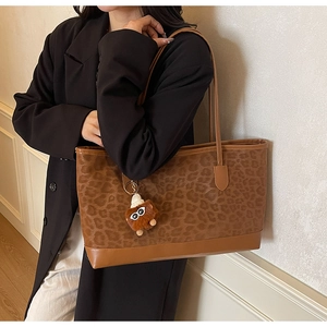Brown leopard print tote bag with plush monster charm worn by a model in black blazer