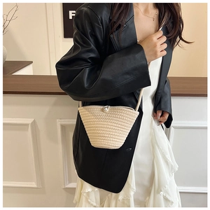 Detail of a beige woven bucket bag featuring a large pearl clasp and thin shoulder strap