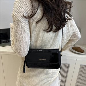Minimalist black patent leather square crossbody bag with gold logo shown on model back