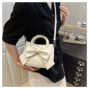 Detailed side view of white faux leather crossbody bag featuring a large decorative bow