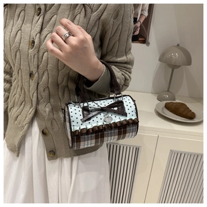 Détail du sac polochon en toile à carreaux avec nœud marron, volants et breloque