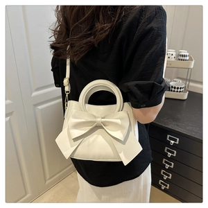 Detail of white PU leather crossbody bag featuring a large decorative bow and gold hardware