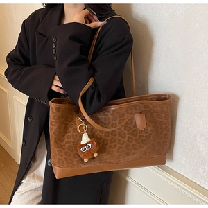 Detail of leopard print tote bag with plush charm on a model in a black coat