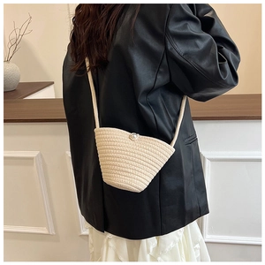 Detail of a beige woven straw bucket bag with a decorative pearl button closure