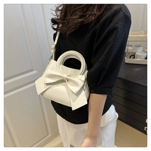 Close-up of white leather crossbody bag featuring a large decorative bow and gold hardware