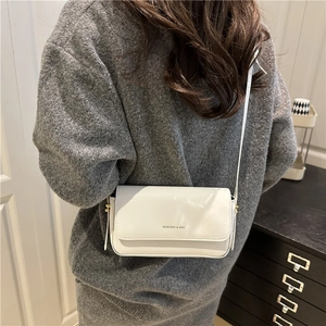 Minimalist white square crossbody bag with glossy finish shown in a stylish street style view