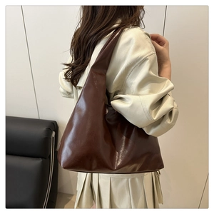 Detail of a brown glossy leather tote bag showing drape and capacity on a model shoulder