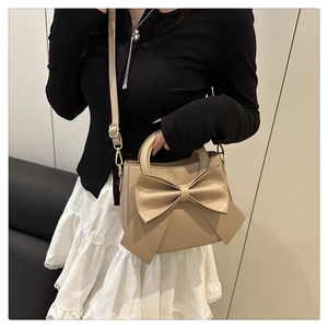 Close-up of a cream crossbody bag featuring a large decorative bow and adjustable strap