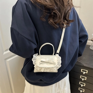White mini PU shoulder bag with lace trim and bow detail worn cross-body