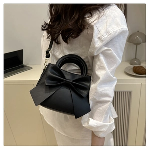 Detail of elegant black crossbody bag featuring a large decorative bow and gold metal hardware