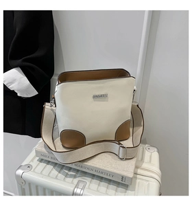 Detail of cream leather shoulder bag with wide strap on travel suitcase