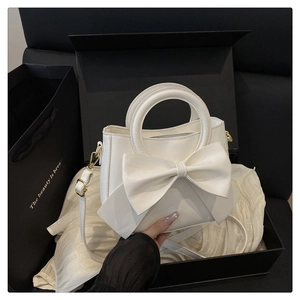 Detail of white handbag with large 3D bow, round handle and gold hardware in a gift box