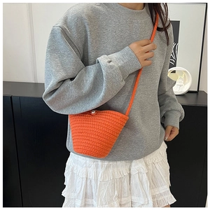 Detail of bright orange knitted bucket bag featuring a white pearl button and crossbody strap