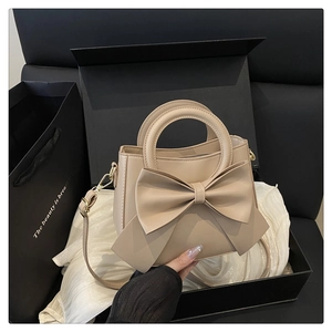 Detailed shot of a beige bow-knot crossbody bag in a black gift box packaging