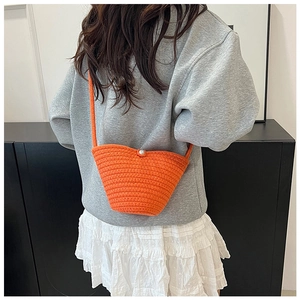 Detailed close-up of an orange woven bucket bag with a pearl button and cross-body strap