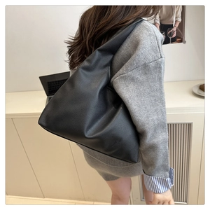Side view of large black pebble leather tote bag worn by model in office setting